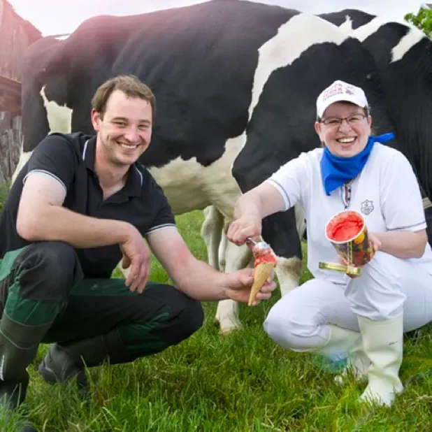A pair of farmers with ice cream in front of a cow.