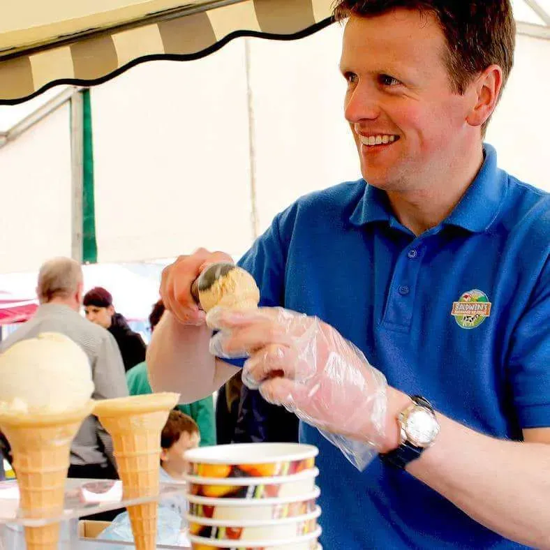 A smiling person making ice cream standing in an ice cream cart.