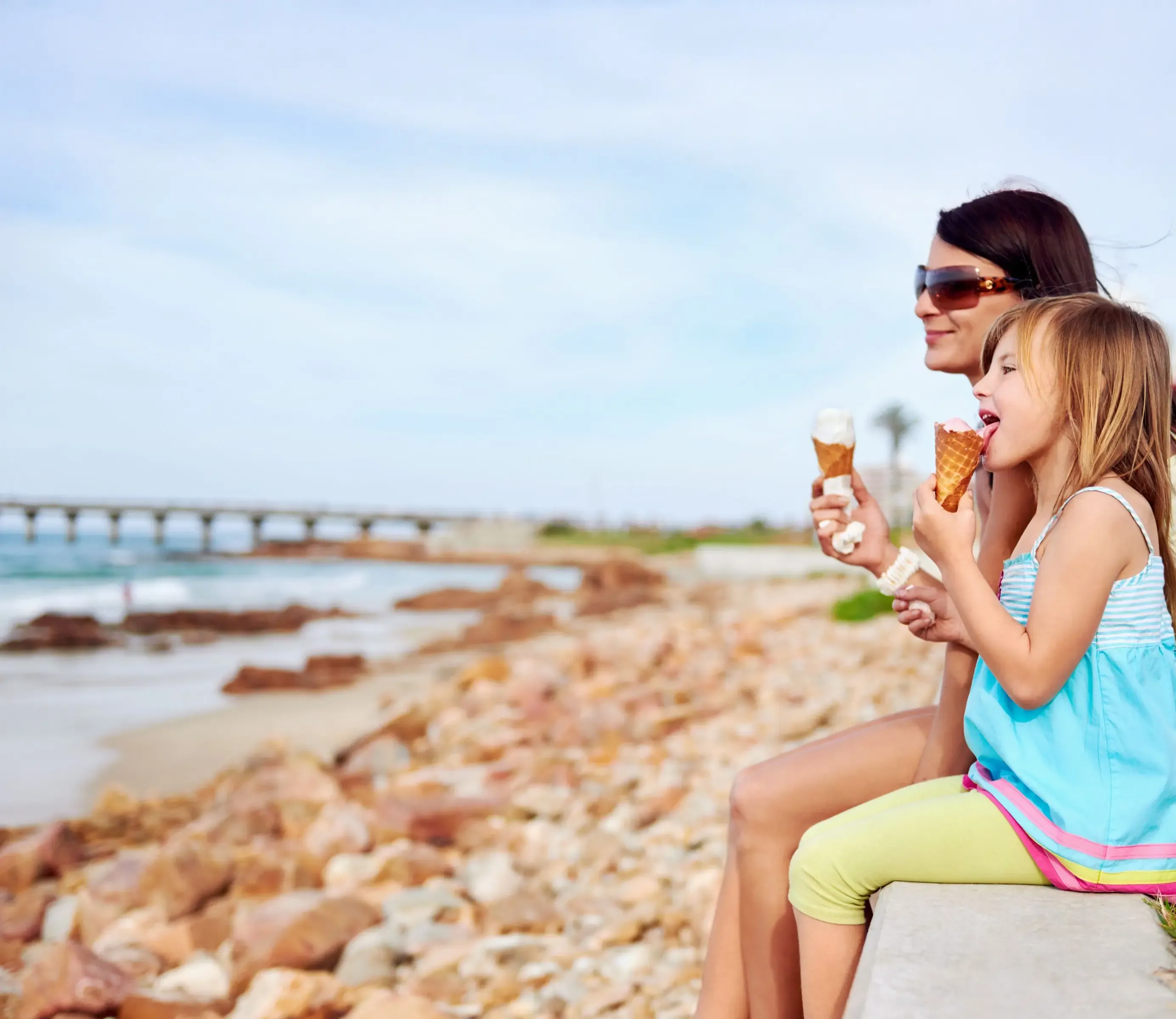 A mother and her daughter enjoying ice cream at the beach.